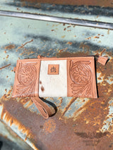 Image of the front side of option B of yipee kiyay clutch wallet with veggie tan leather that is stamped with a floral design on each side with white cowhide with some brown speckles in the middle with a leather patch with STS branded into it.